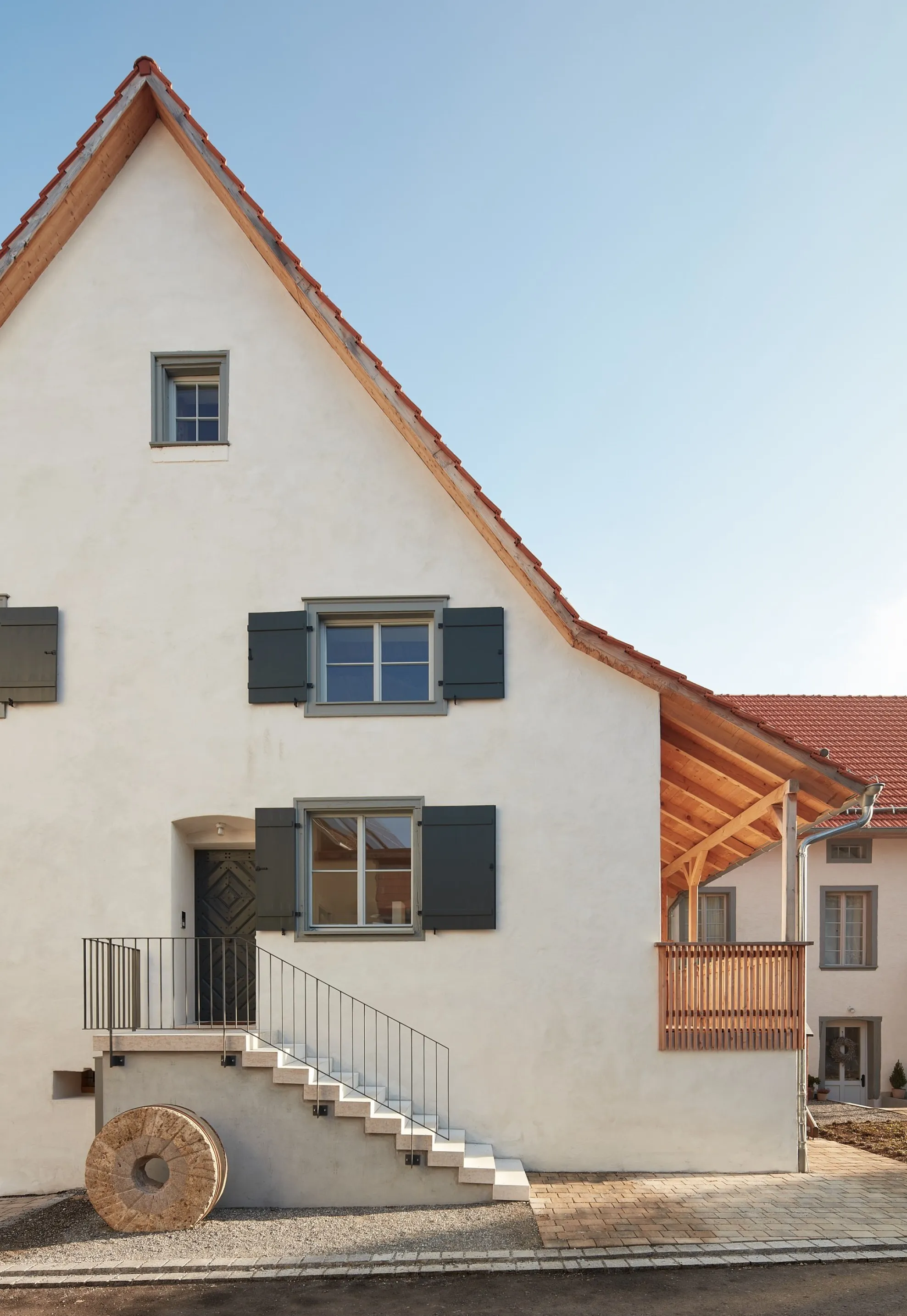 Saniertes denkmalgeschütztes Mühlengebäude in Aach. Giebelfassade mit weißem Putz, Biberschwanzziegeln und grünen Fensterläden, Außentreppe und altem Mühlrad