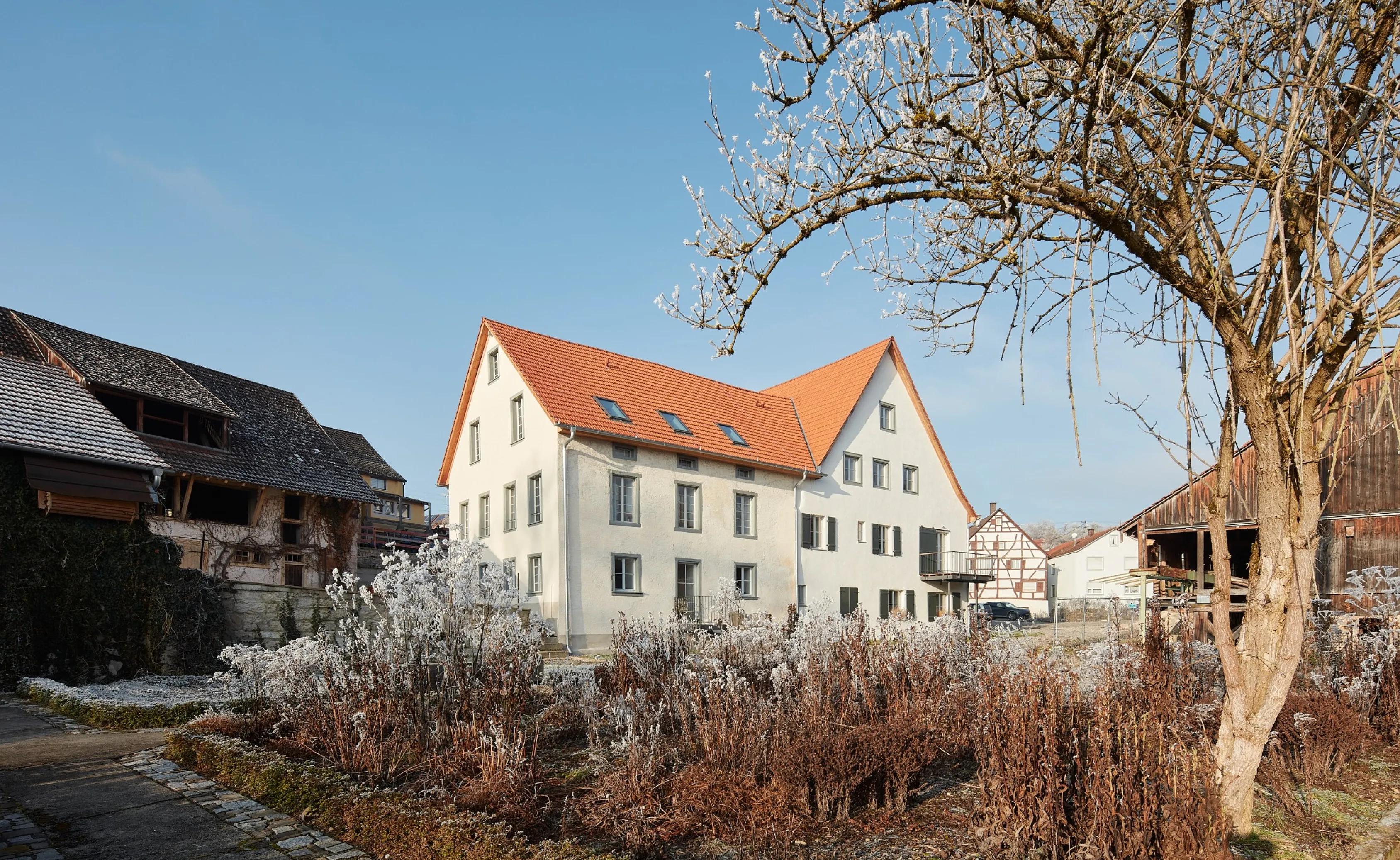 Saniertes denkmalgeschütztes Mühlengebäude in Aach mit weißem Putz, Biberschwanzziegeln und grünen Fensterläden eingebunden in die winterliche Umgebung