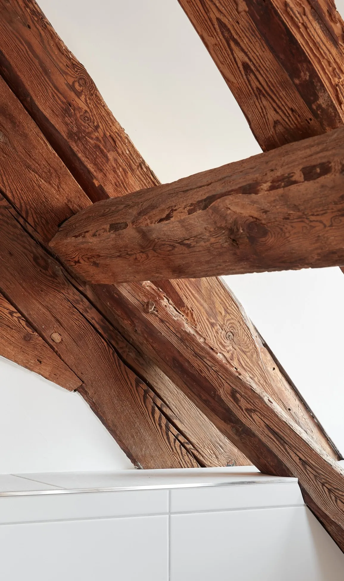 Innenansicht des Anschlussdetails der weißen, großformatigen Fliese zur historischen Balkenlage