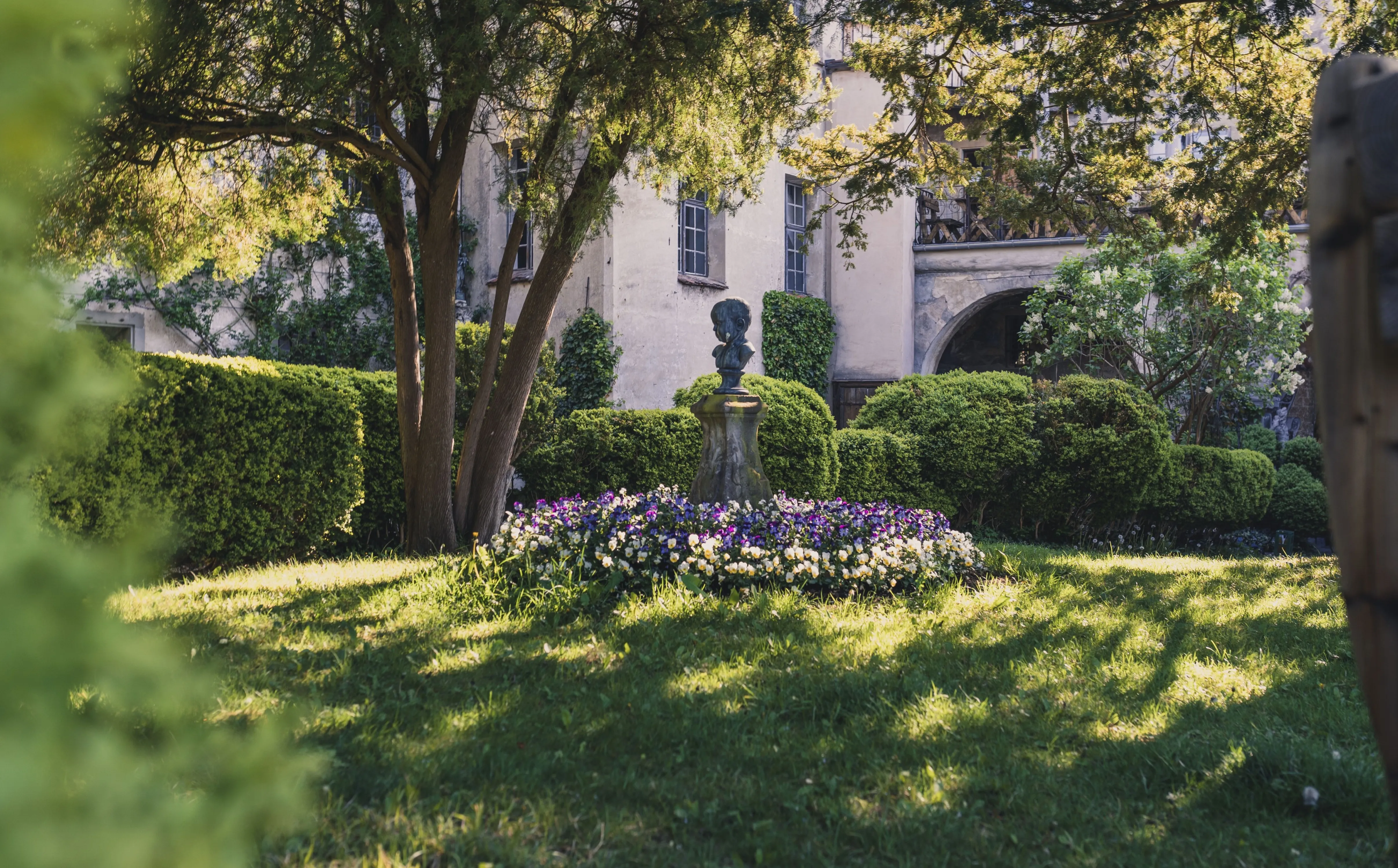 Garten der Burg Meersburg mit blühenden Pflanzen und Skulptur