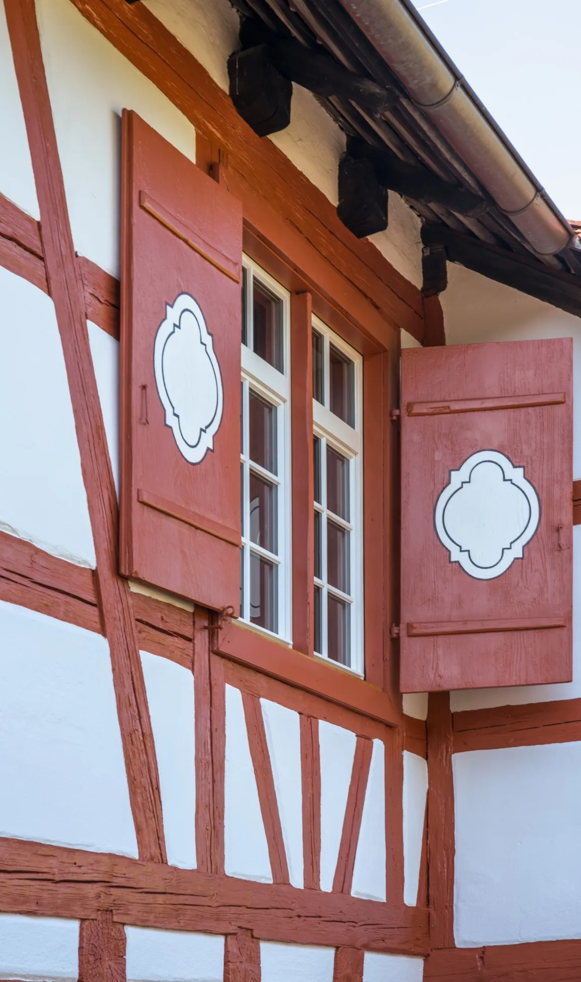 Detailansicht der Fassade und Fenster. Rotes Fachwerk, weißes Gefach, weiße Fenster und mit weißem Ornament versehene Fensterläden