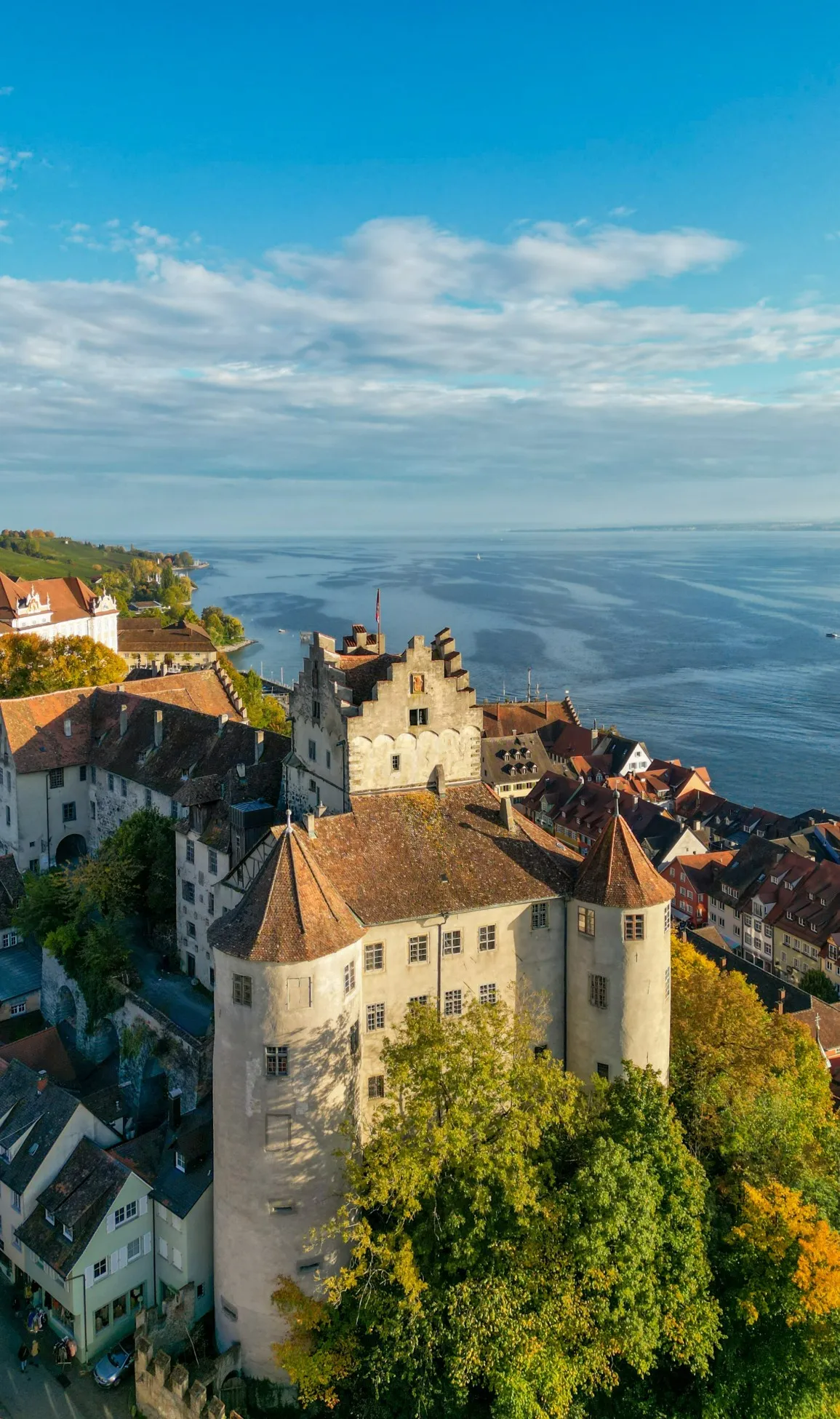 Luftbildaufnahme der Burg Meersburg im Herbst bei Sonnenuntergang. Im Hintergrund die Stadt Meersburg und der Bodensee.