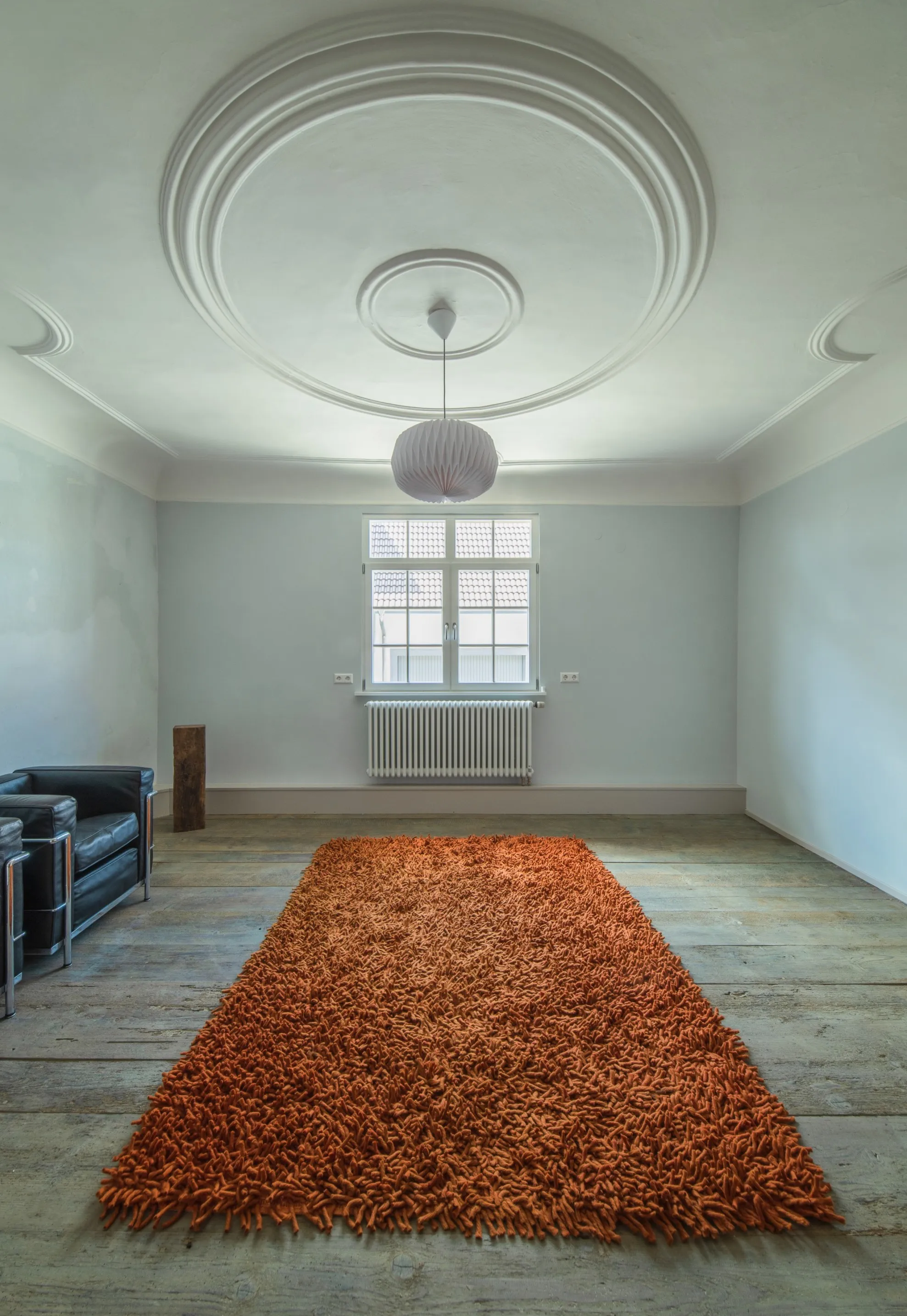 Innenraumansicht des Wohnzimmers mit Altbau-Stuckdecken, hellblauen Innenwänden, orangenem Teppich und zwei Cassina LC2 Sesseln von Le Corbusier